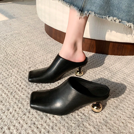 Black high-heeled shoes with gold accents worn by a person sitting on a chair.
