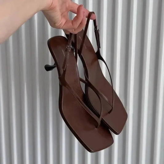 Brown sandals held by a hand against a neutral background