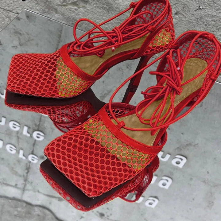 Red high-heeled sandals with mesh design on a reflective surface.