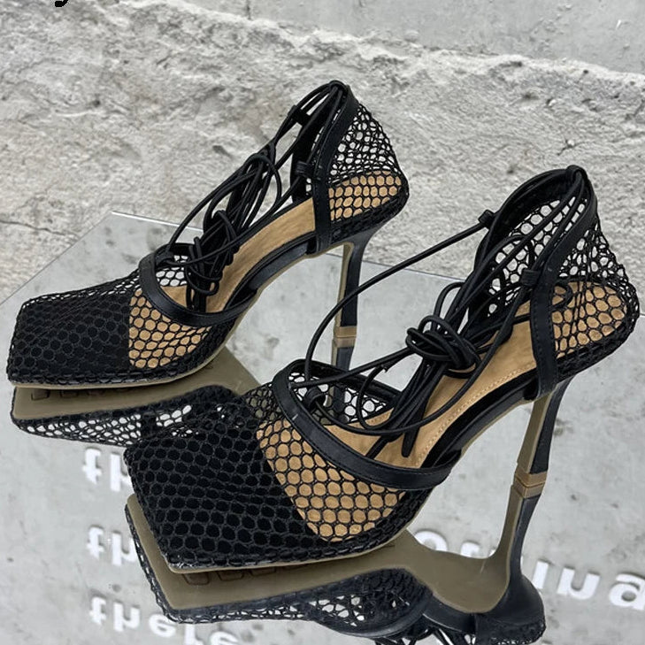 Black high-heeled shoes with mesh design on a gray surface