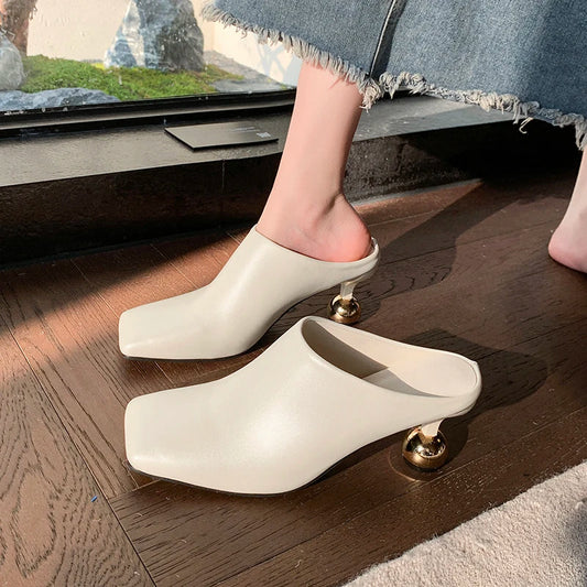 White clogs with gold accents worn indoors on a wooden floor.