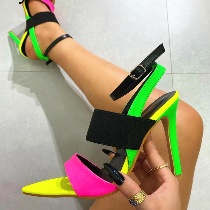 Neon green, pink, and black high-heeled sandals being worn on a light gray floor.