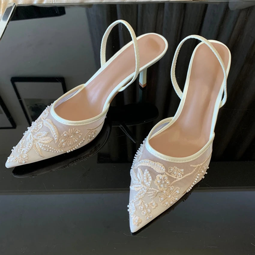 Pair of white lace high-heeled shoes on a black surface