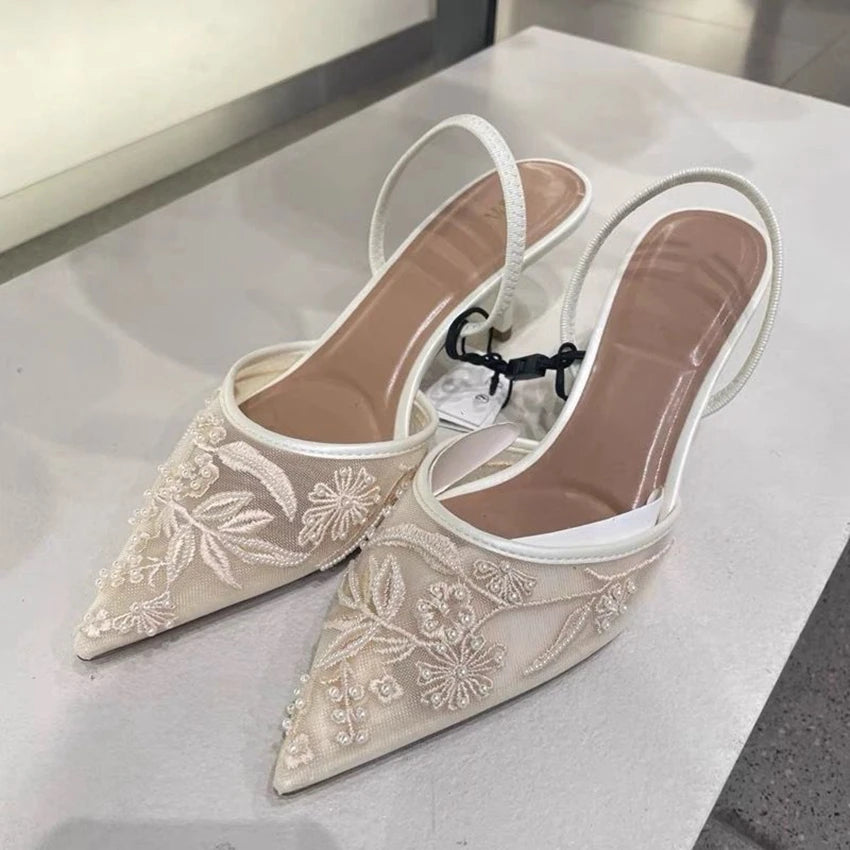 Pair of beige pointed-toe shoes with floral embroidery on a light gray surface.